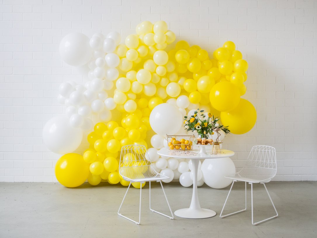 Mit Orangen und Leckereien gedeckter Tisch mit weißen und gelben Luftballons im Hintergrund
