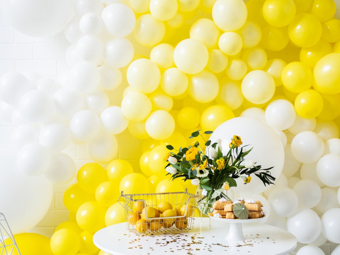 Mit Orangen und Leckereien gedeckter Tisch im Detail mit weißen und gelben Luftballons im Hintergrund