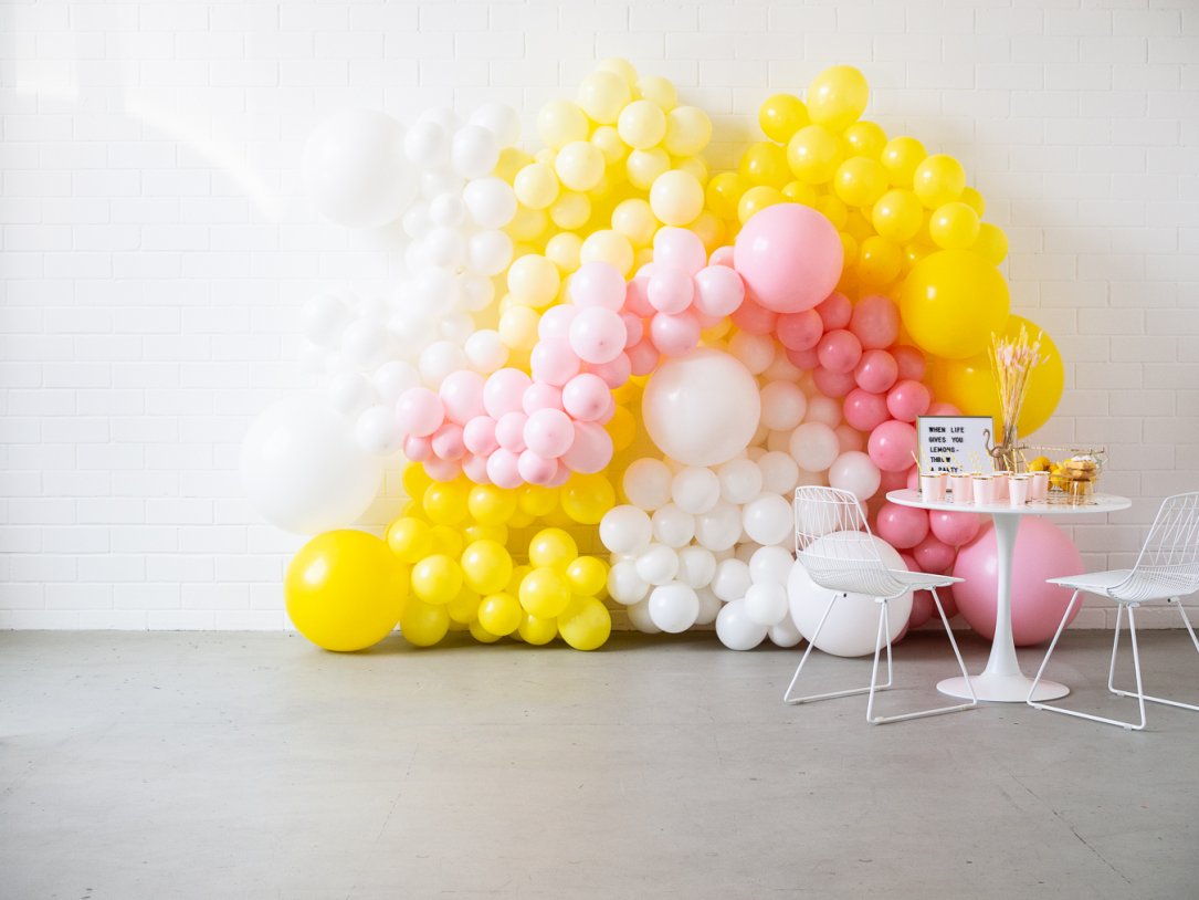 Dekorierter Limonadenstand mit dem Spruch "When Life gives you lemons - throw a party" und mit weißen, rosafarbenen und gelben Luftballons im Hintergrund