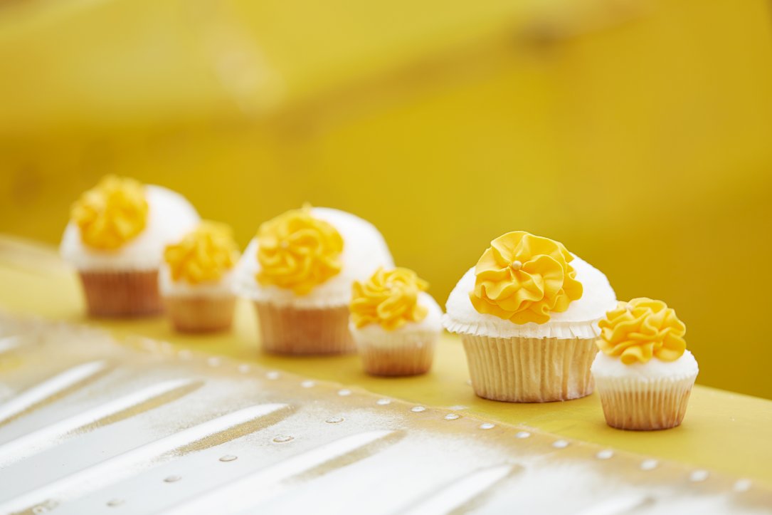 Unterschiedliche große Muffins mit gelben Blüten dekoriert und gelbem Hintergrund