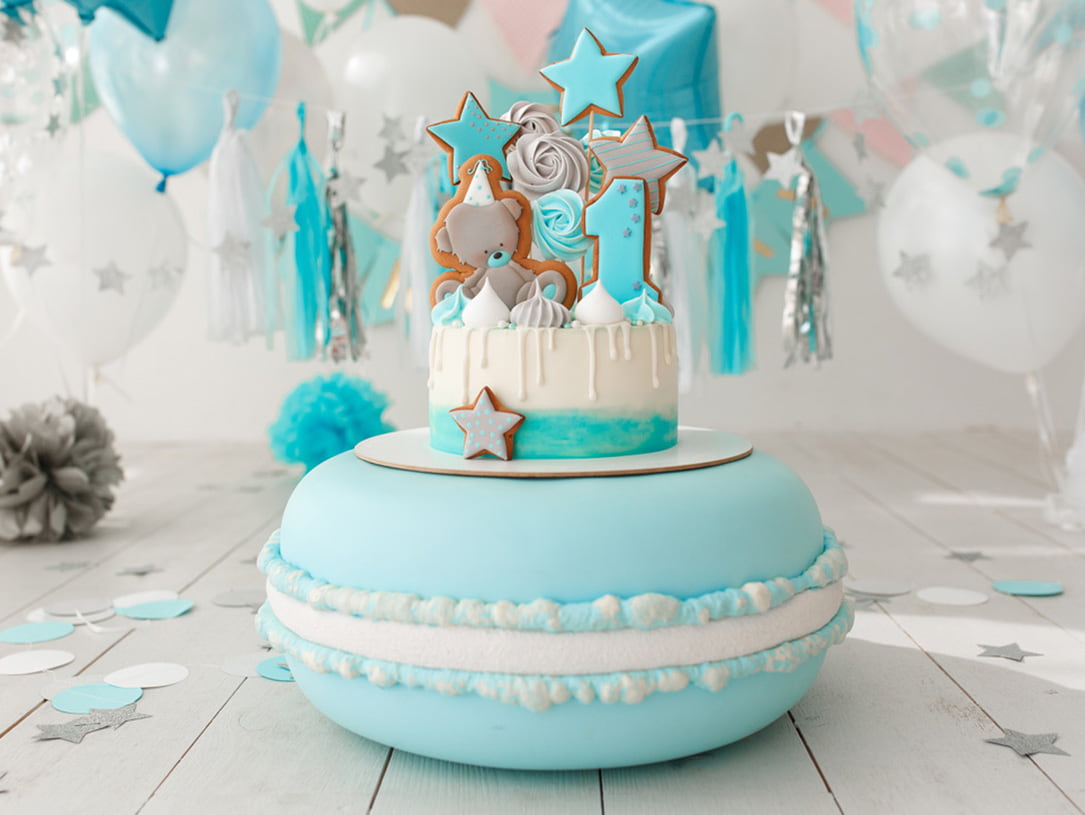 Torte in Macarons-Optik mit Teddybär- und Sternendekor sowie Luftballons im Hintergrund in Blautönen