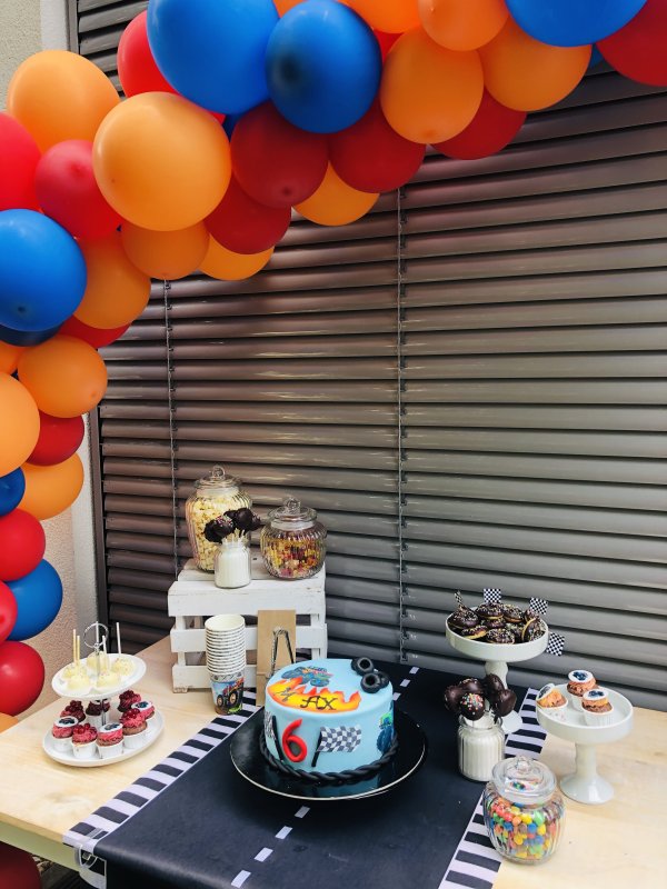 Torte, Donuts, Gummibärchen und weitere Leckereien auf einem Tisch mit blauen, roten und orangefarbenen Luftballons darüber