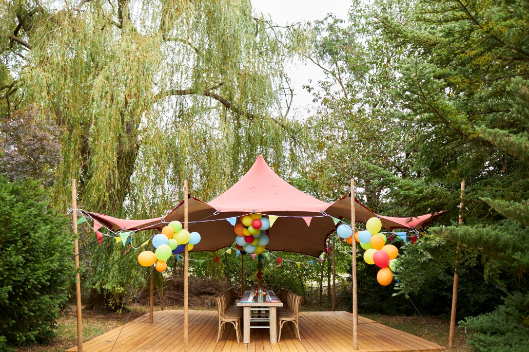 Bunt geschmückte Tafel mit Holzmöbeln und Zelt mit vielen bunten Luftballons im Freien aus der Ferne