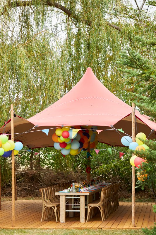 Bunt geschmückte Tafel mit Holzmöbeln und Zelt mit vielen bunten Luftballons im Freien aus der Ferne