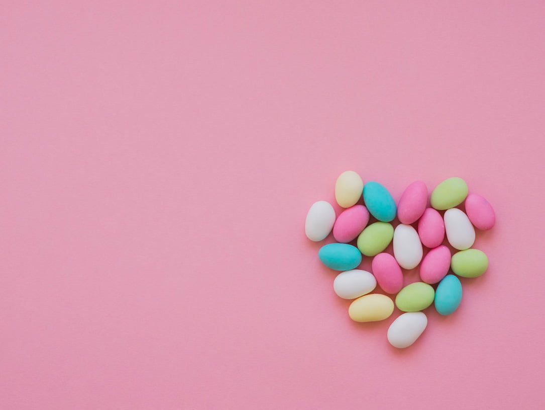 Herzform gelegt aus bunten Bonbons auf einem rosafarbenen Hintergrund